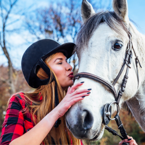 Woman kissing a white horse in an outdoor setting